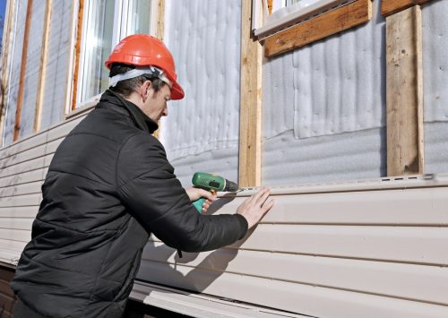 worker installs beige vinyl siding