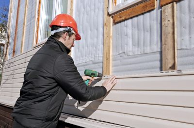 worker installs beige vinyl siding