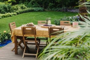 Dining table covered with orange tablecloth standing on wooden terrace in green garden